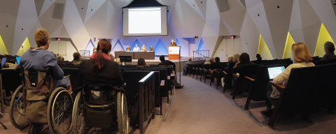 People with and without disabilities attentively listen to a presentation at a conference.