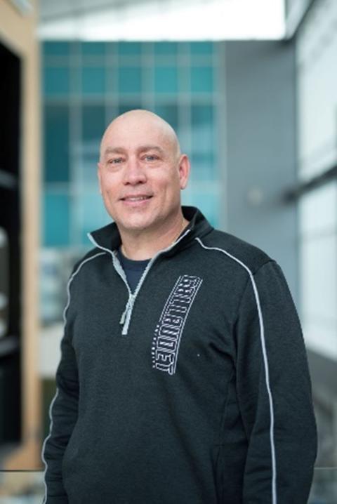 Russ Stein is a light skinned man with a shaved head wearing a black Gallaudet windbreaker
