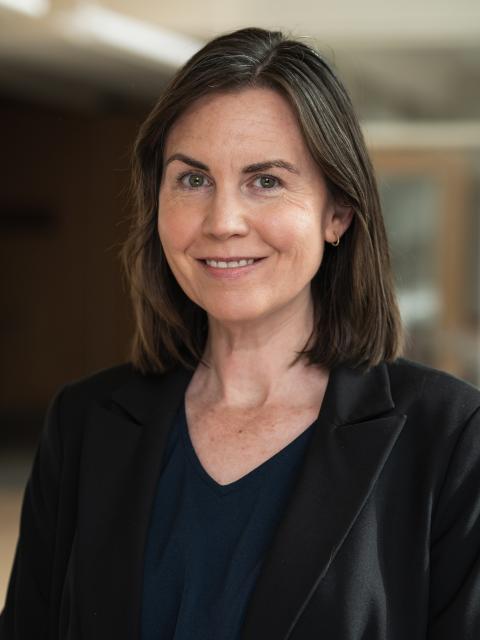 Megan Henly is a professionally dressed woman with shoulder-length styled brown hair.